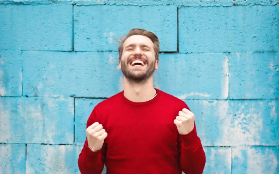 Man in a red sweater celebrating a big win with both fists up