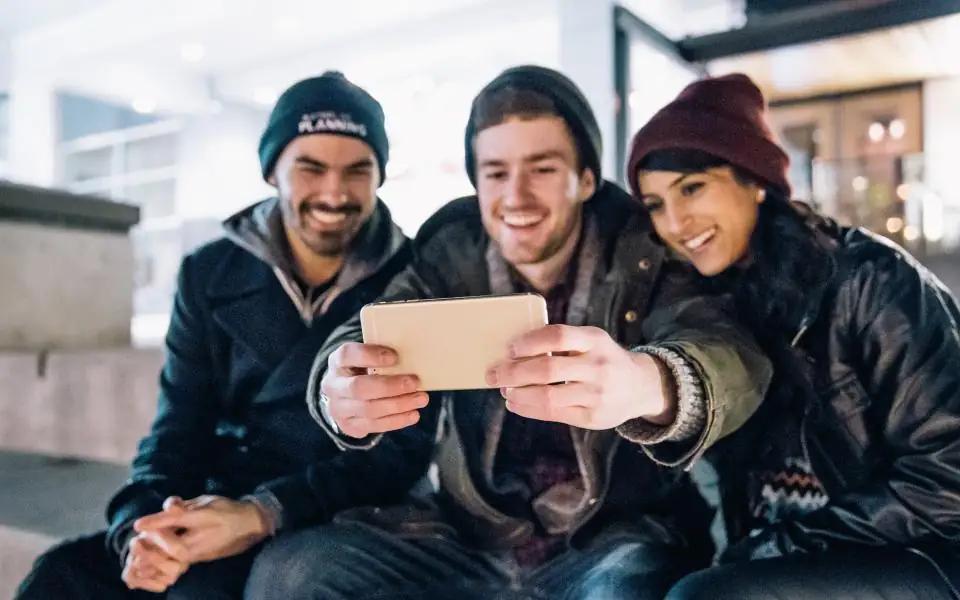 Three friends laughing while checking JLBETPH games on a smartphone